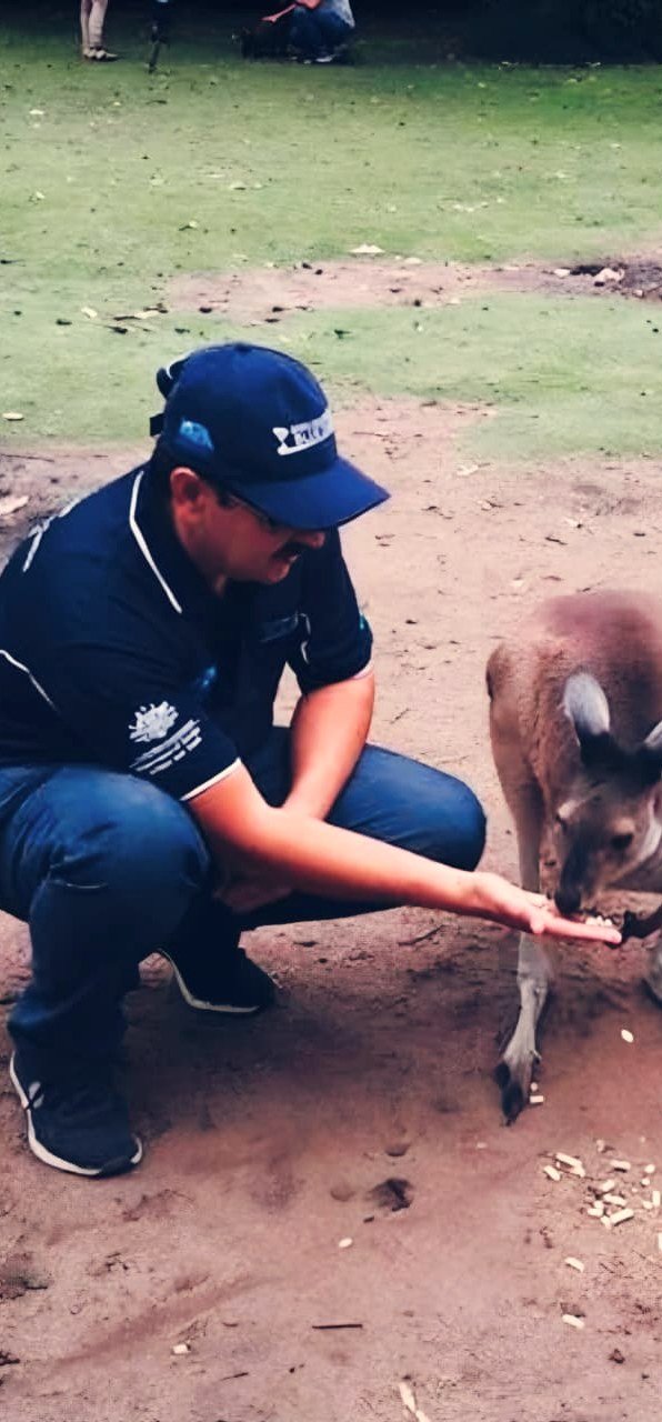 Bilal Anwar crouching to feed a kangaroo from his open hand at a wildlife park