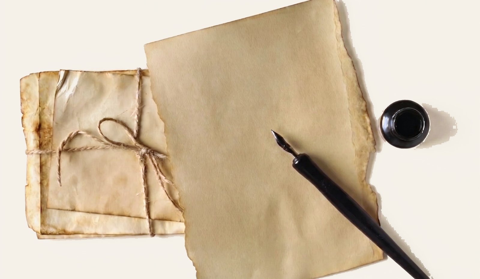 A letter tied with twine, a sheet of writing paper, a fountain pen and an ink pot on a desk