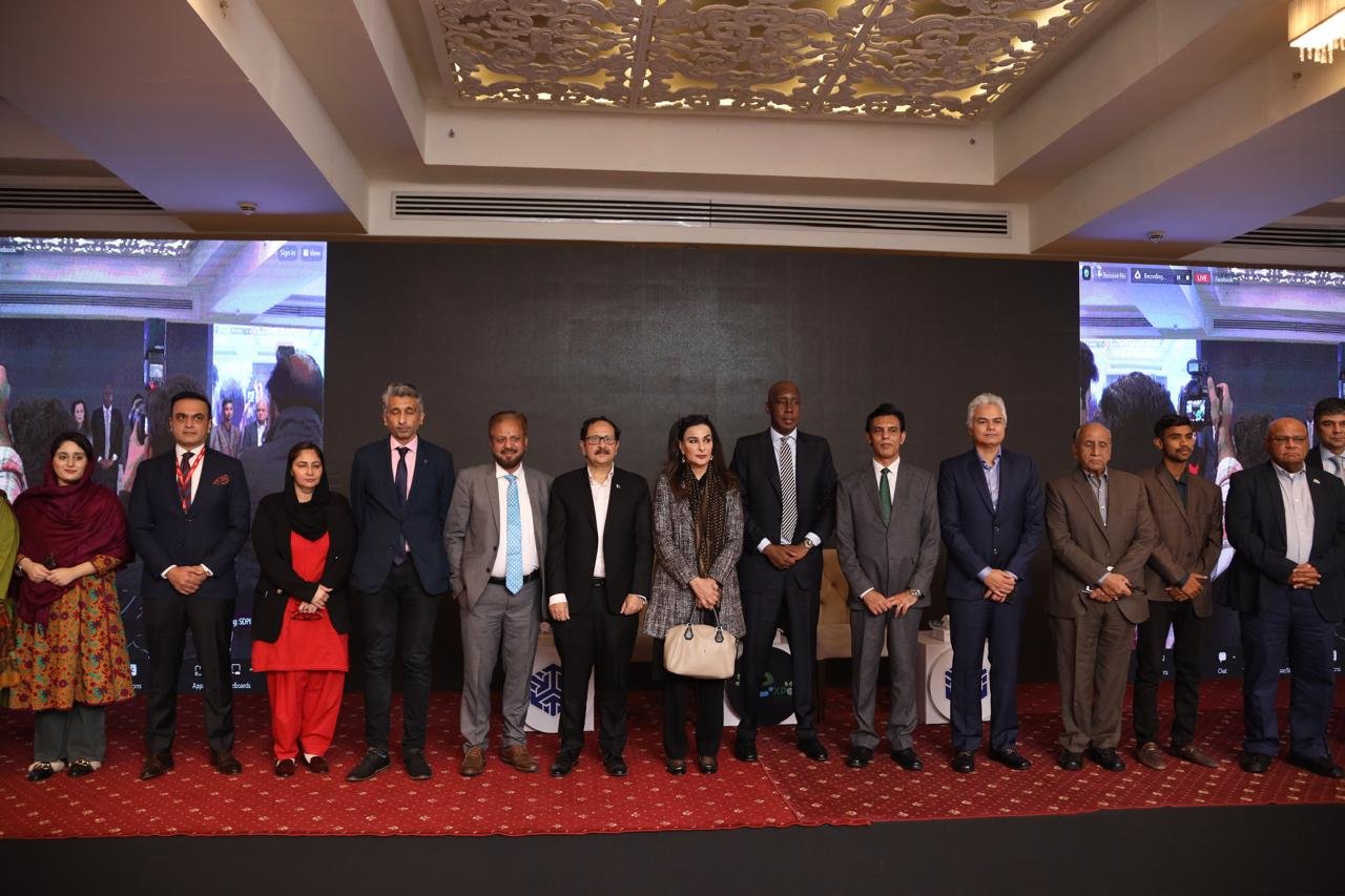 A line of speakers and delegates on stage for a group photograph at the close of a conference session