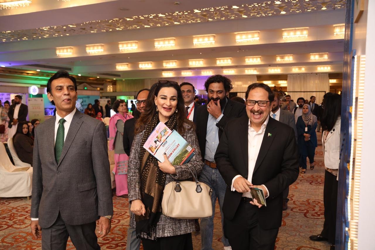 Bilal Anwar walking the floor of a sustainable development expo with a delegation, publications in hand