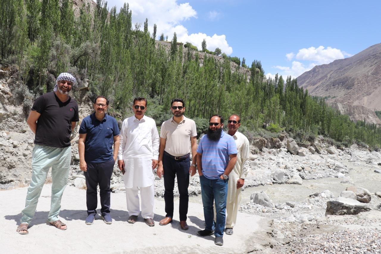 A team standing on a boulder-strewn riverbed in a northern valley, poplars and bare mountainside behind